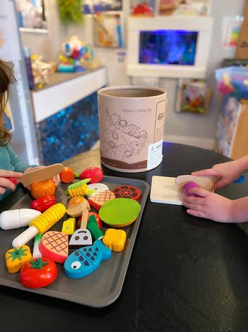 Reviewer's photo of a child slicing a pretend wooden veggie with a tray of the pretend foods sitting on the table