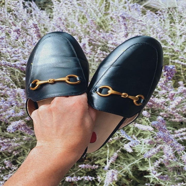 a reviewer holding the loafer mules in black, showing the gold chain and open back