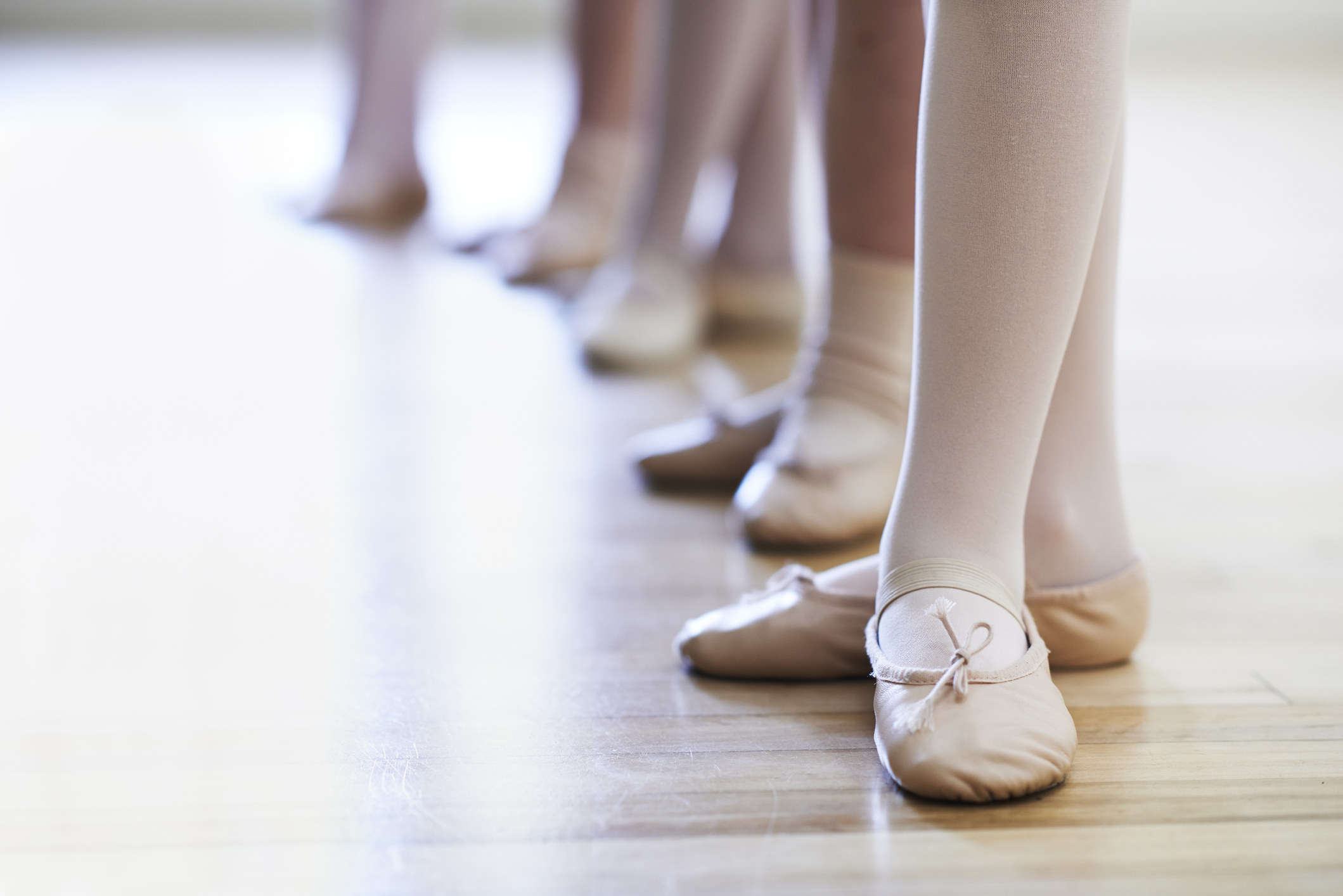 Close up of dancers feet standing in a line, with ballet slippers and tights in in third position.