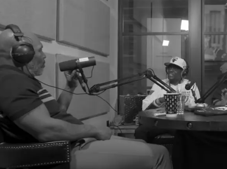Black-and-white image of Mike sitting and talking to Boosie