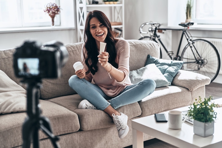 Woman smiling and sitting on a sofa and holding a product in front of a camera
