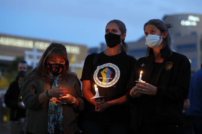 Three people wearing masks stand with candles