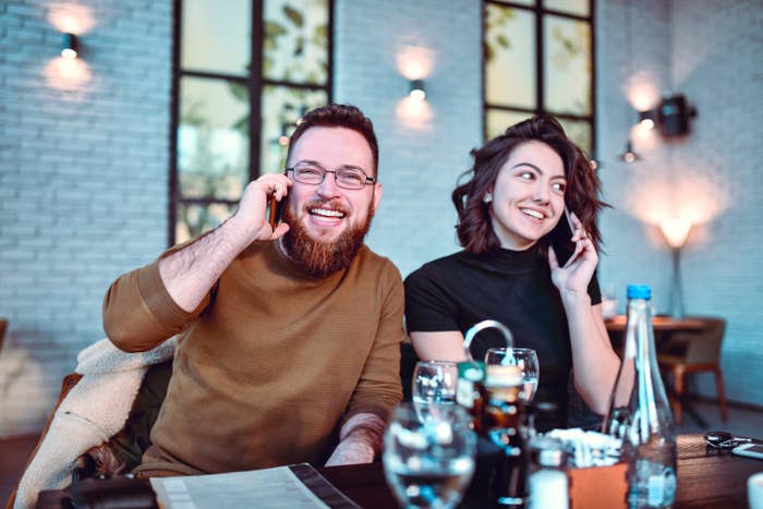 Friends Engaged In Deep Phone Call Conversations At Restaurant Dinner