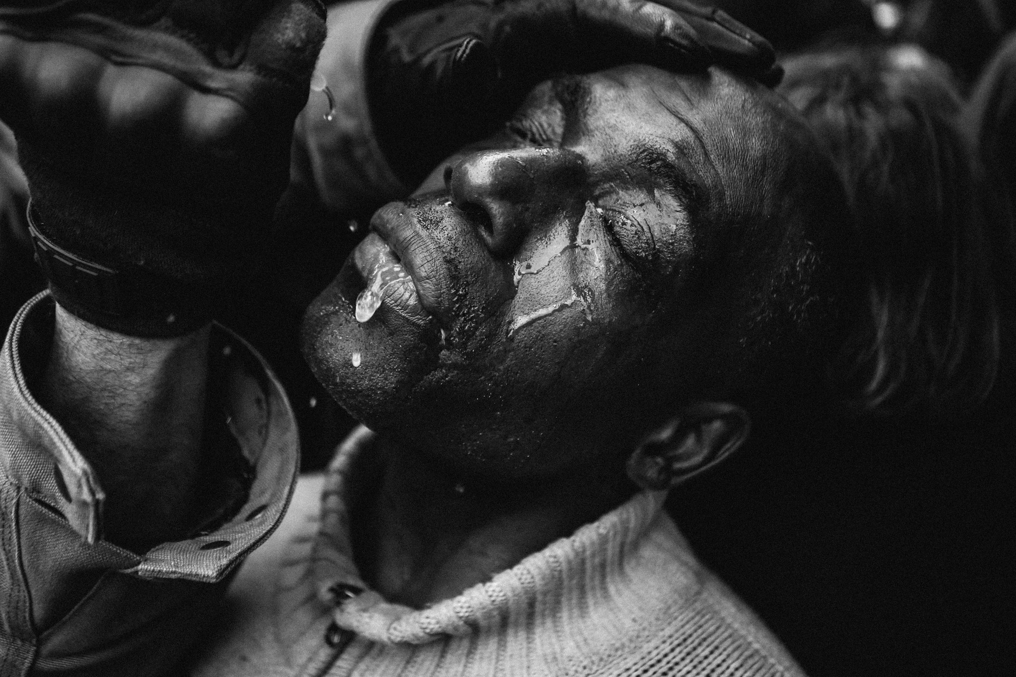 A man has his head tilted back and water poured on his face during a protest