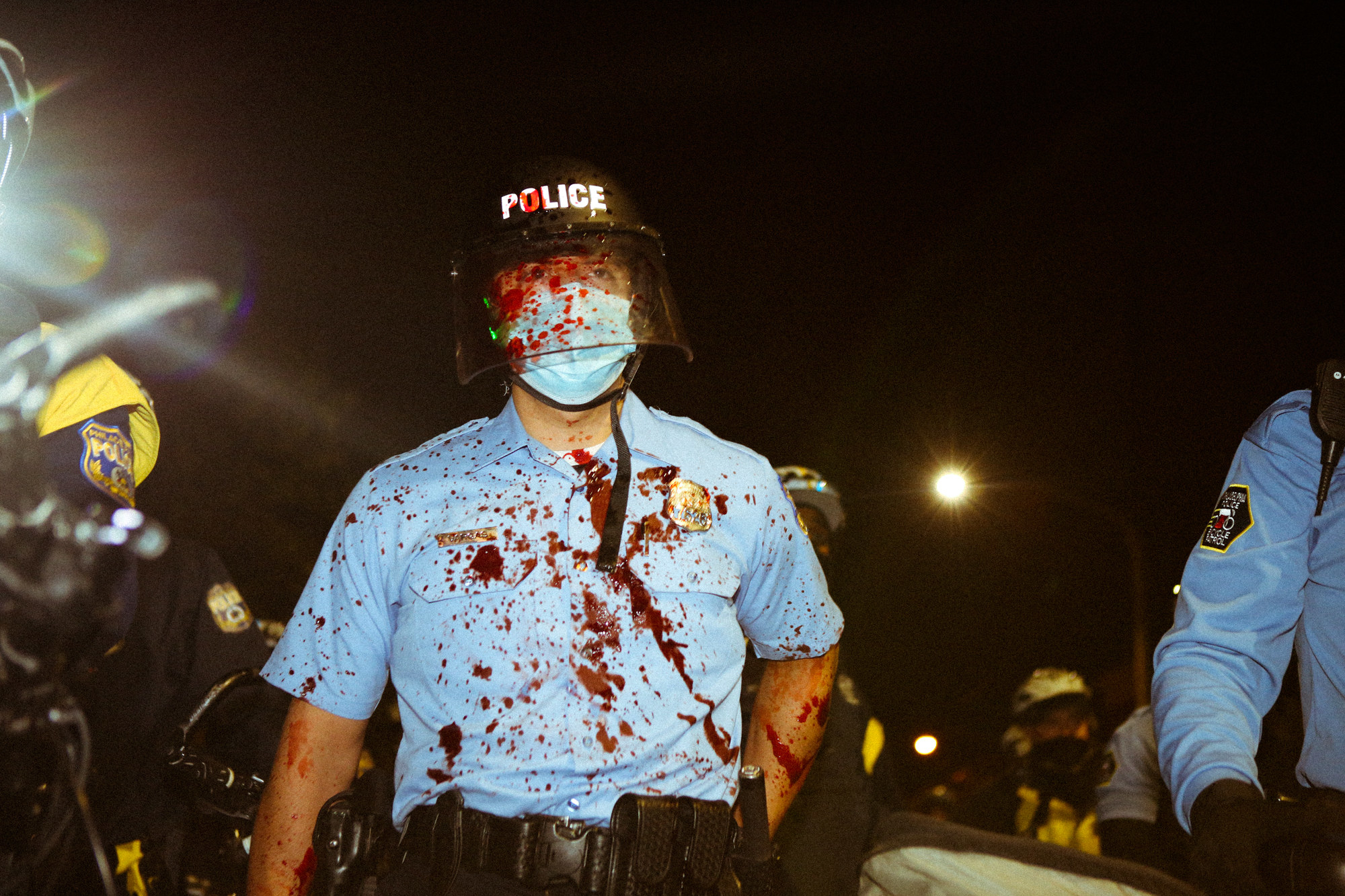 A policeman walking towards the camera, covered in blood