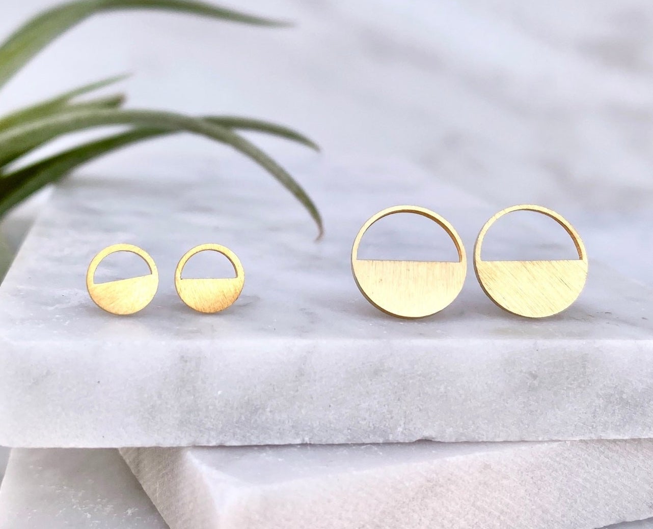 A pair of small and large half-circle stud earrings.