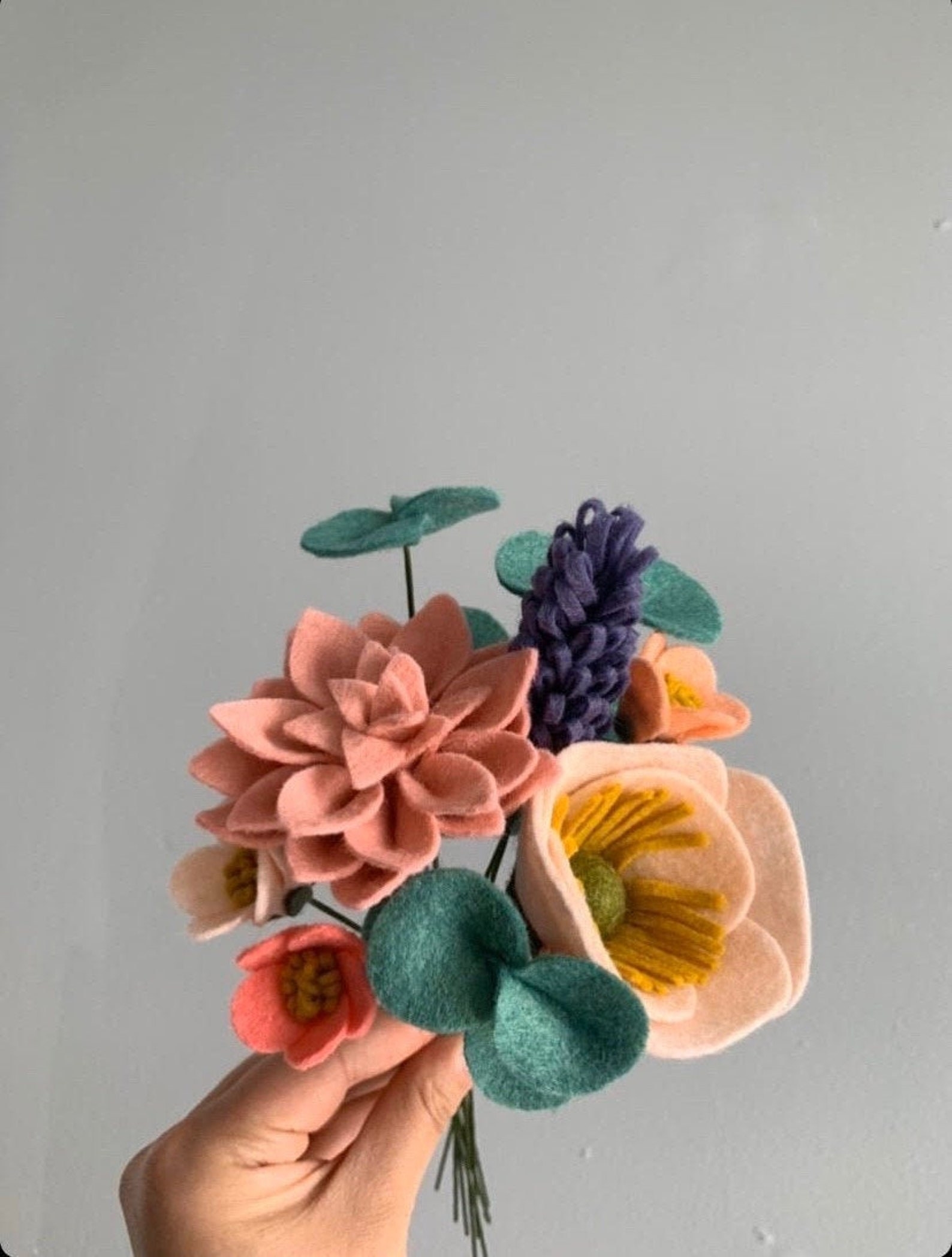 a felt bouquet including green eucalyptus, and pink, coral, red, and pink flowers