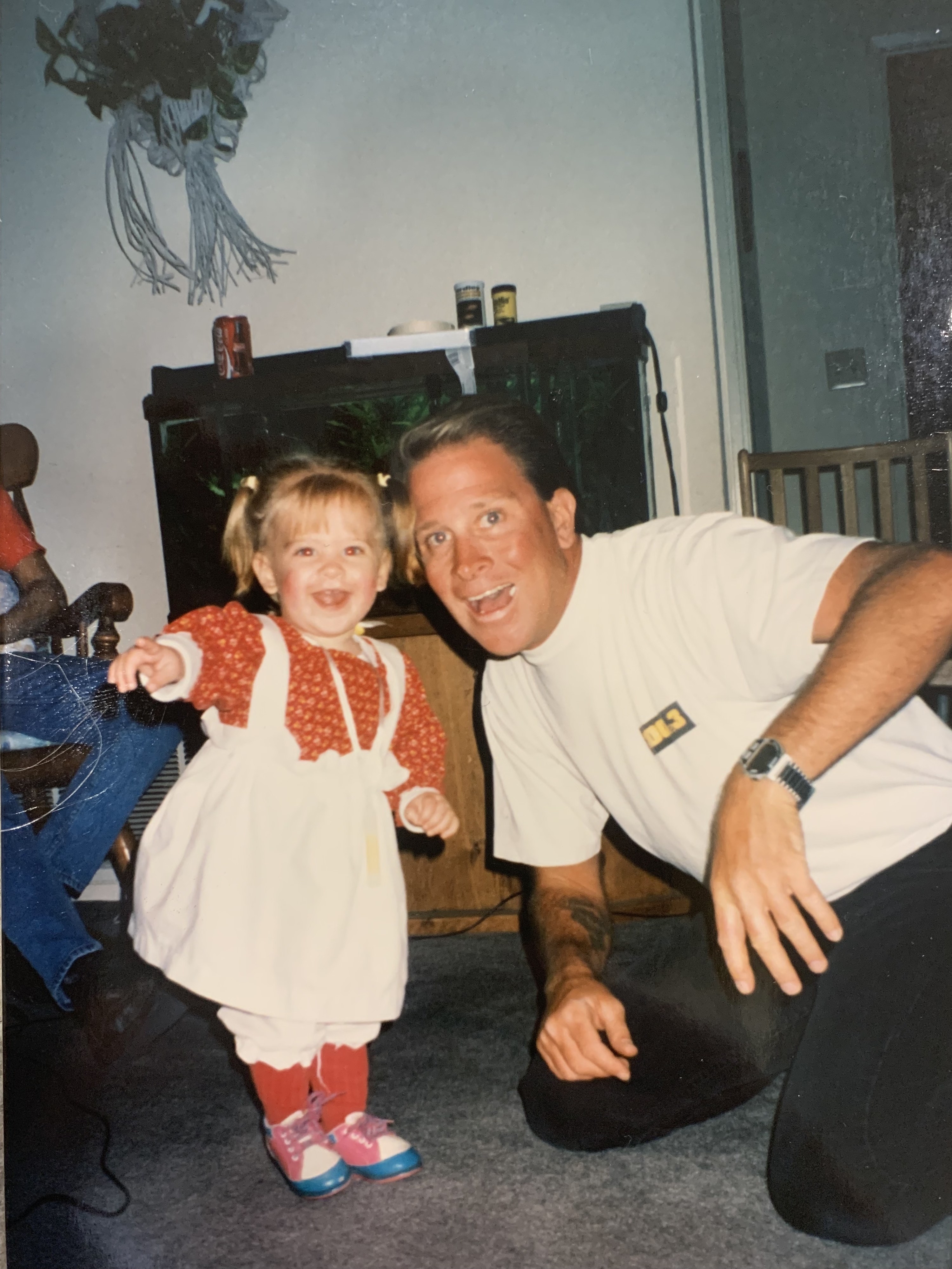 A smiling toddler points at the camera, with her father next to her