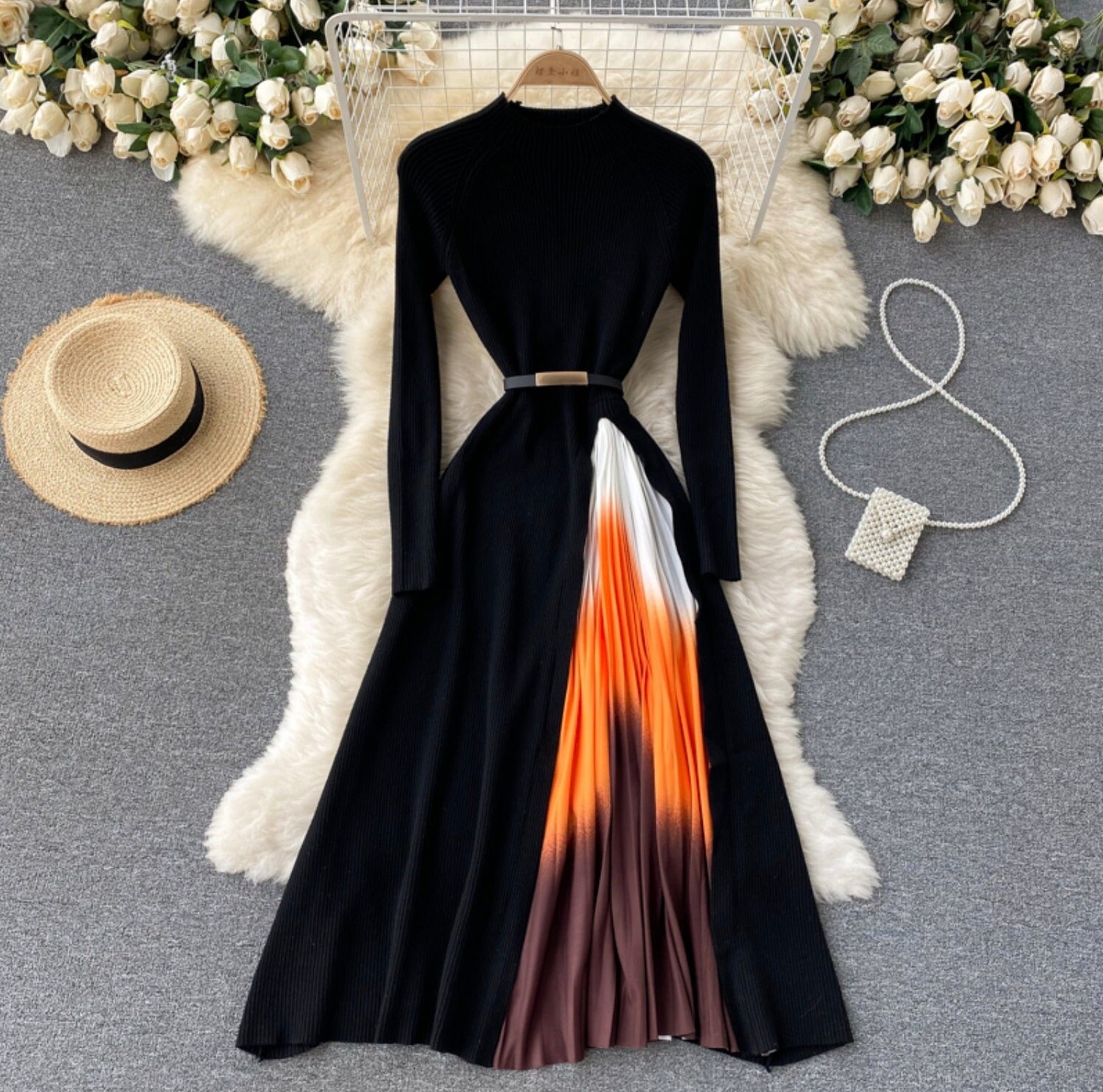 a long sleeve black dress with a belted waist and a pleated insert that&#x27;s white, orange, and brown ombre