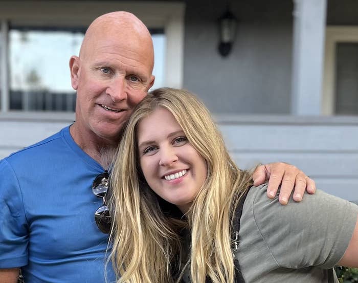 A bald man has his hand on the shoulder of a blonde smiling woman