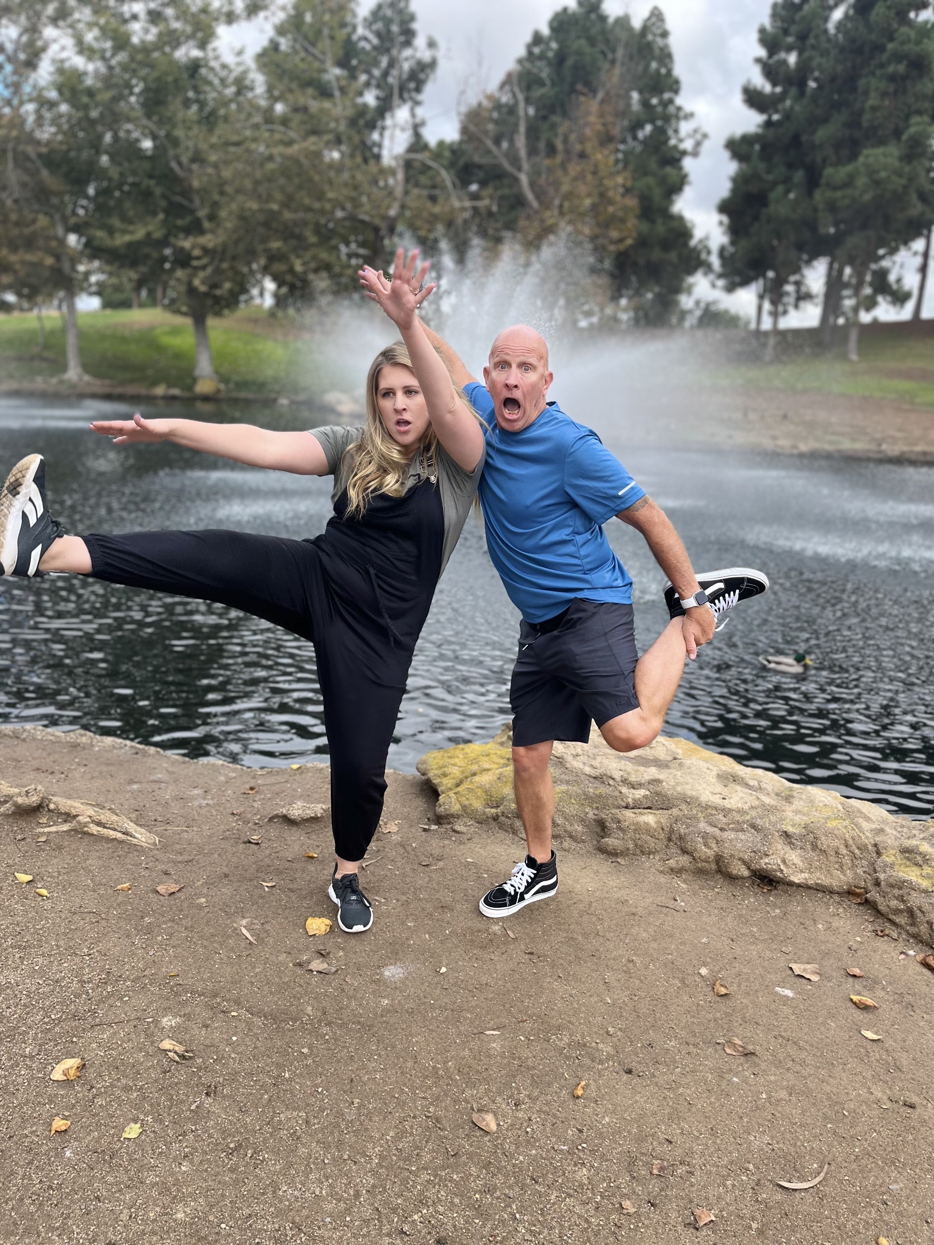 Justine kickes her leg into the air while her dad hops on one foot.