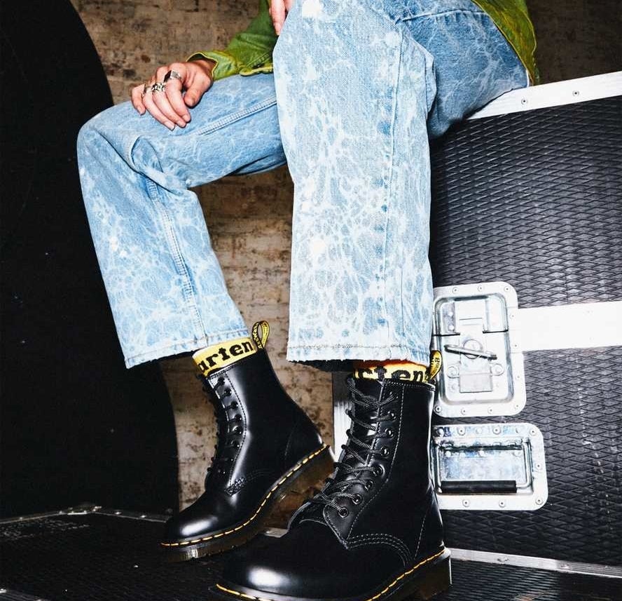Model is wearing black leather combat boots with acid wash denim jeans