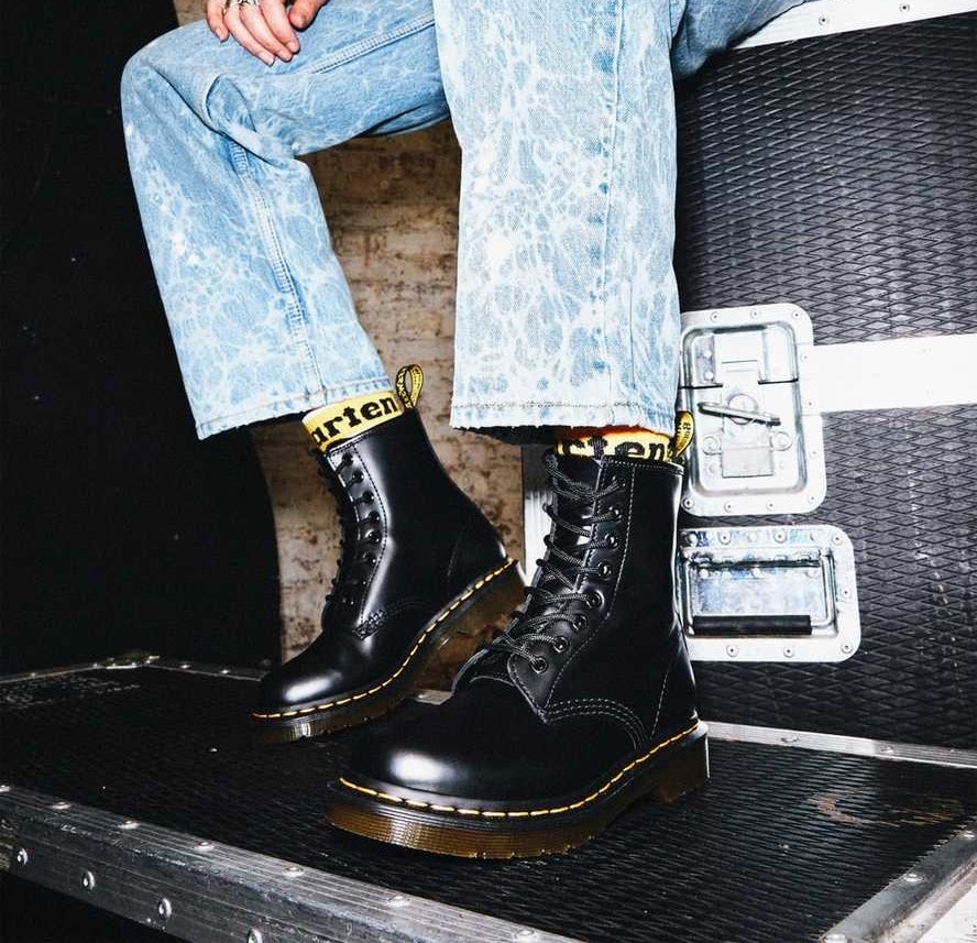 Model is wearing black leather combat boots with acid wash denim jeans