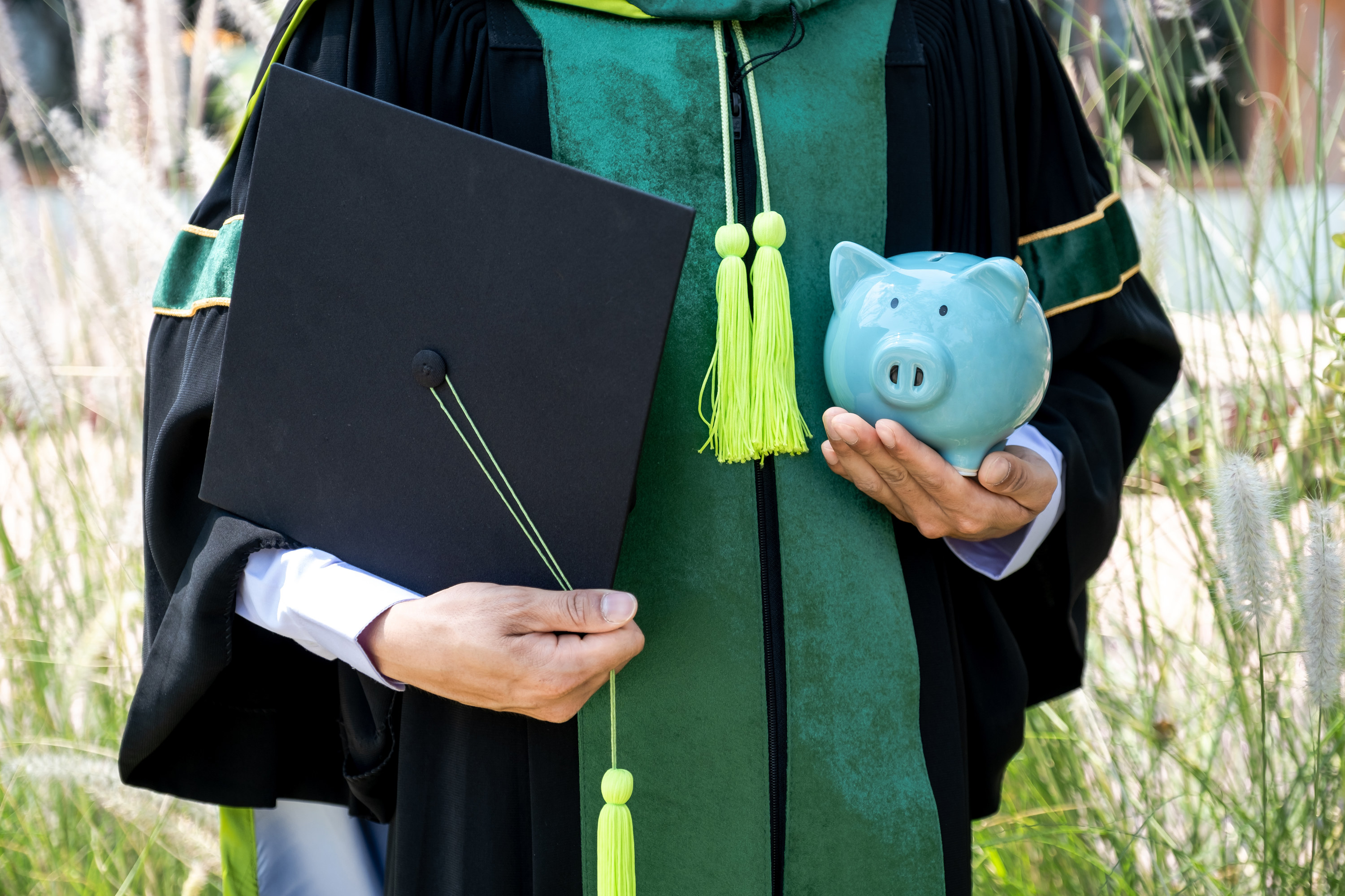Person wearing a cap and gown holding a piggy bank