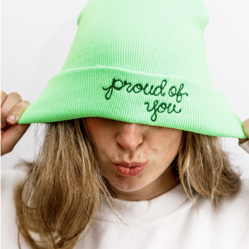 a model in a lime green hat that says &quot;proud of you&quot; in chain link stitching