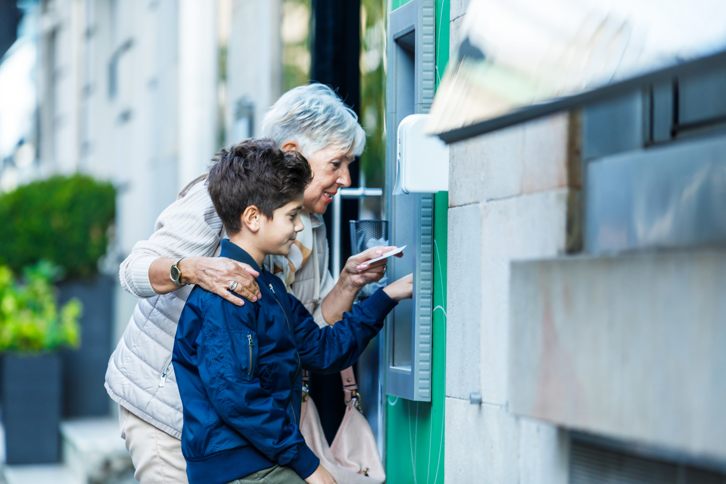 Little boy using an ATM with his grandmother