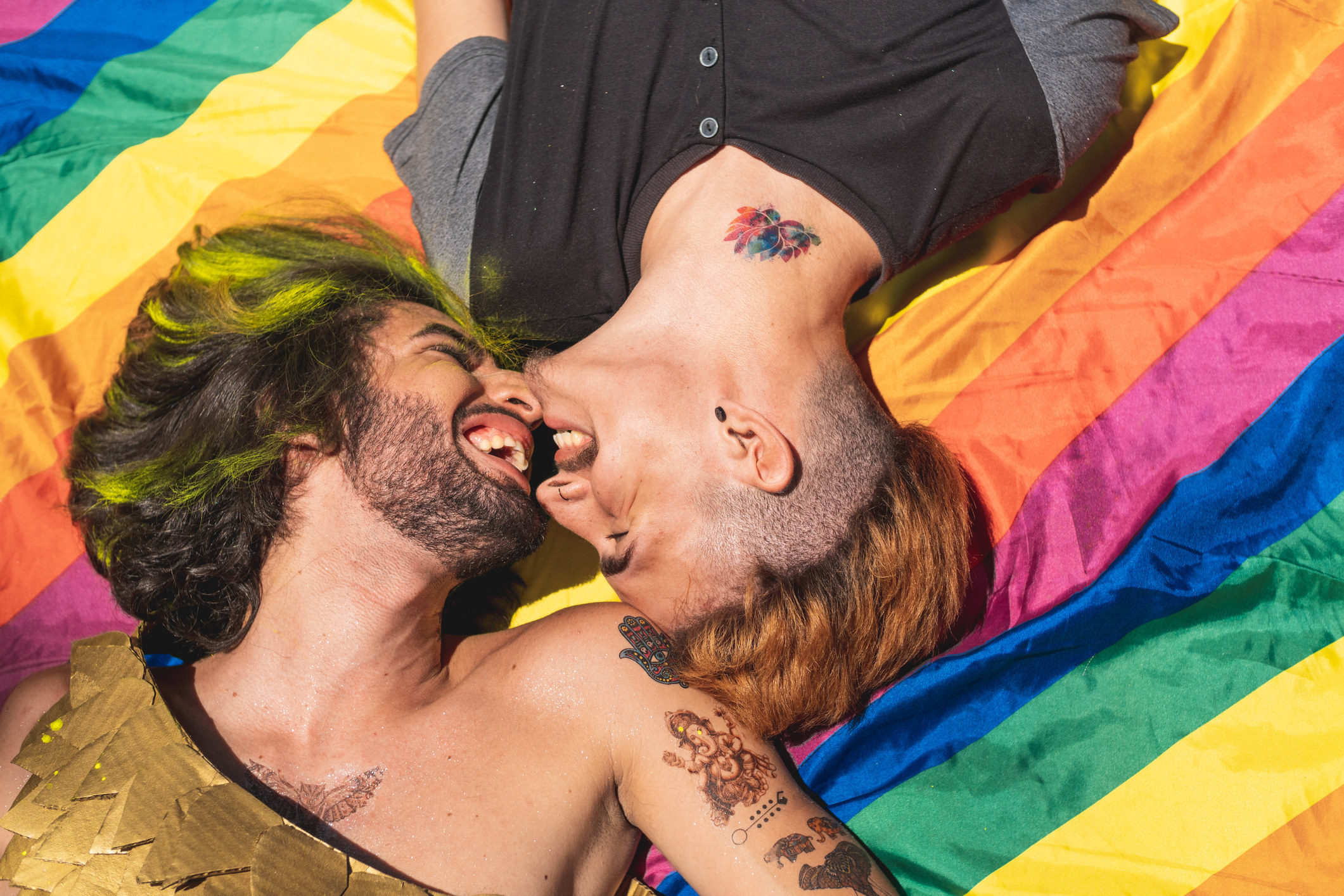 Two men smiling close to each other, lying on a gay flag