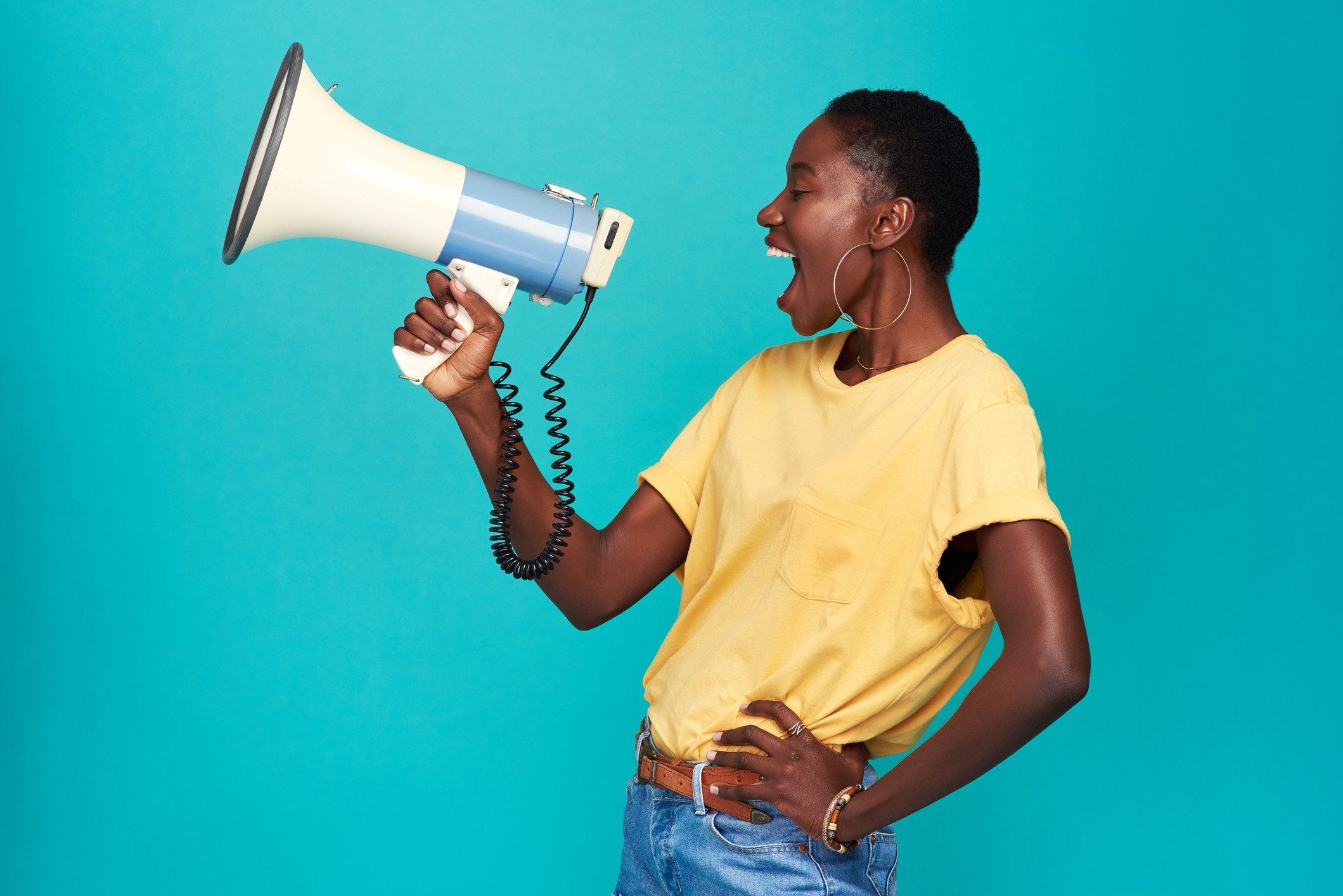 Studio shot of a young woman using a megaphone against a turquoise background