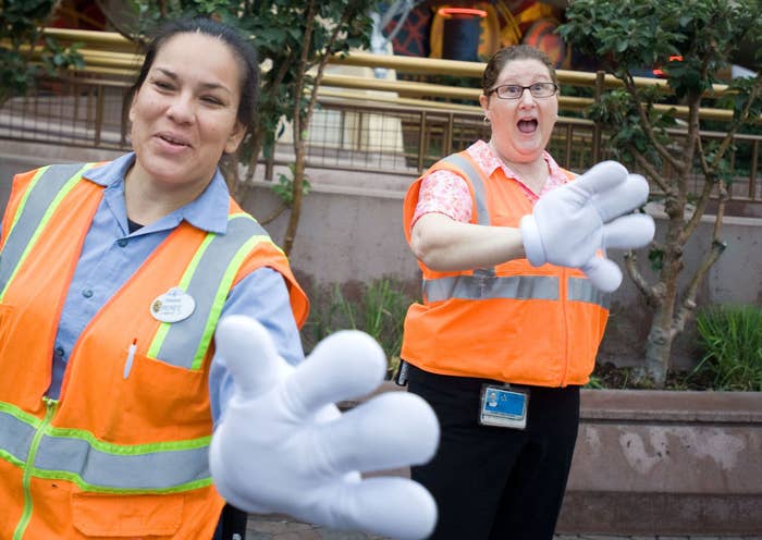 Two Disneyland employees wearing safety vests and holding out their hands with Mickey gloves on to give 5k runners high-fives