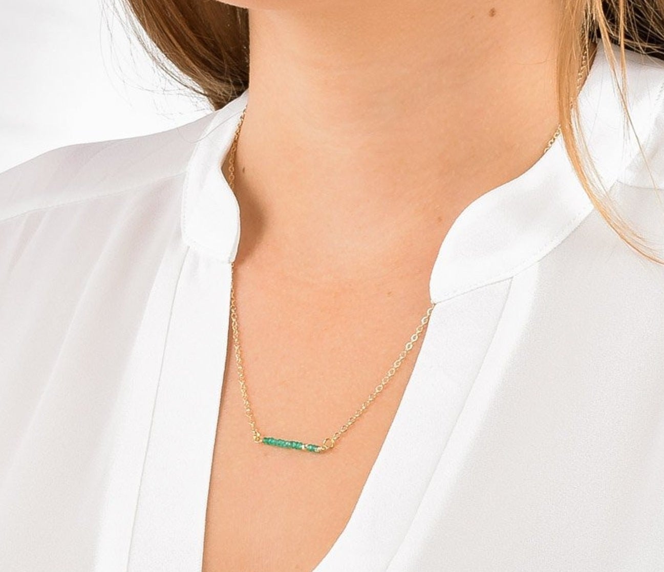 A person wearing a golden chain necklace with a bar of green onyx gemstone beads.