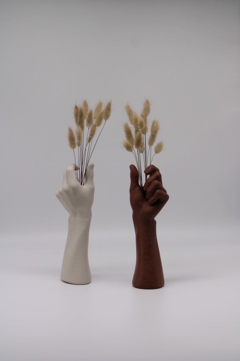 two hand-shaped vases, both holding dried flowers.