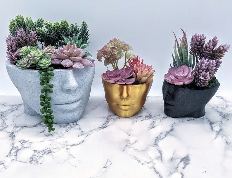 Product image of large marble colored pot, small gold pot, and small black pot in the shapes of faces