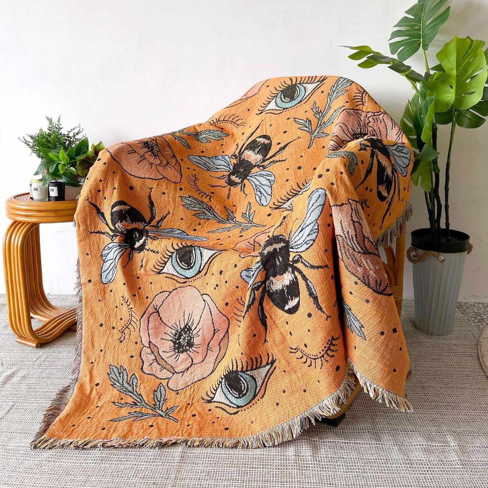 an orange throw blanket with flowers, bees, and eyes