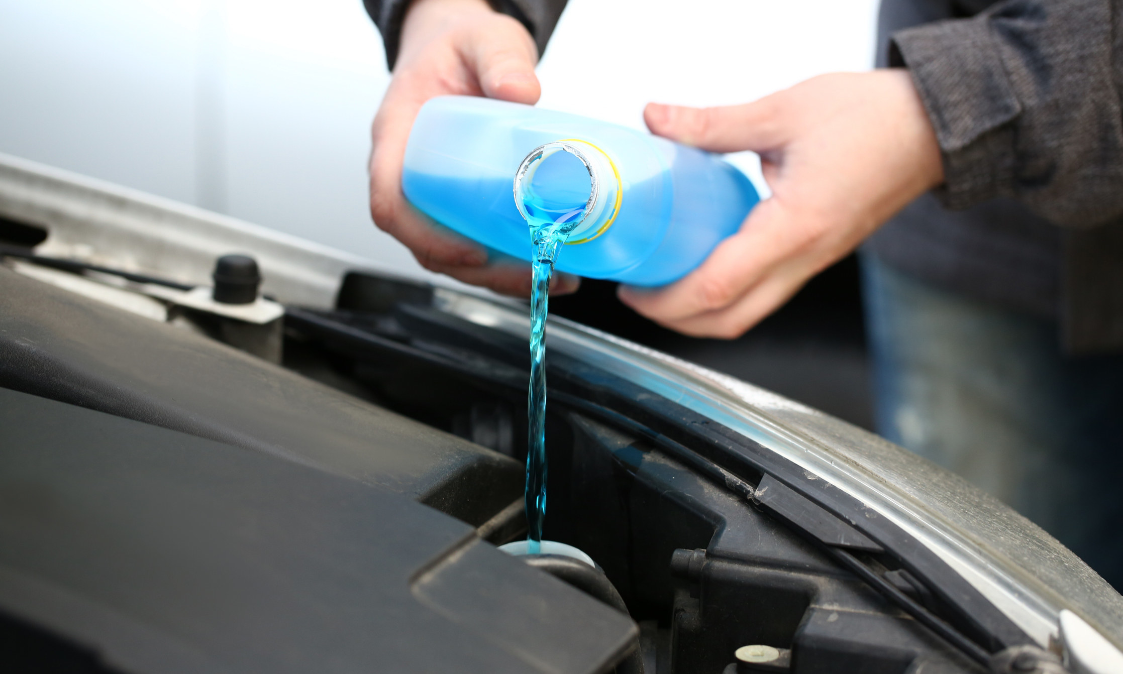 a person pouring blue windshield wiper fluid into their car