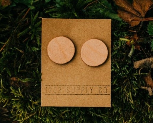 A pair of circular, tan leather earrings.