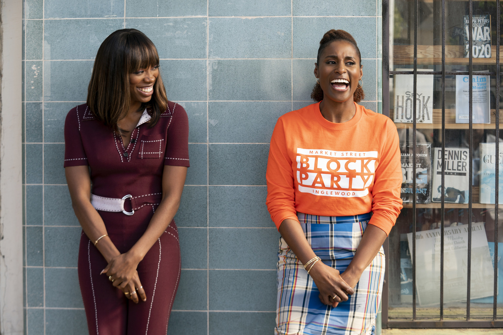 Molly and Issa smiling as they lean against a wall as they stand next to each other