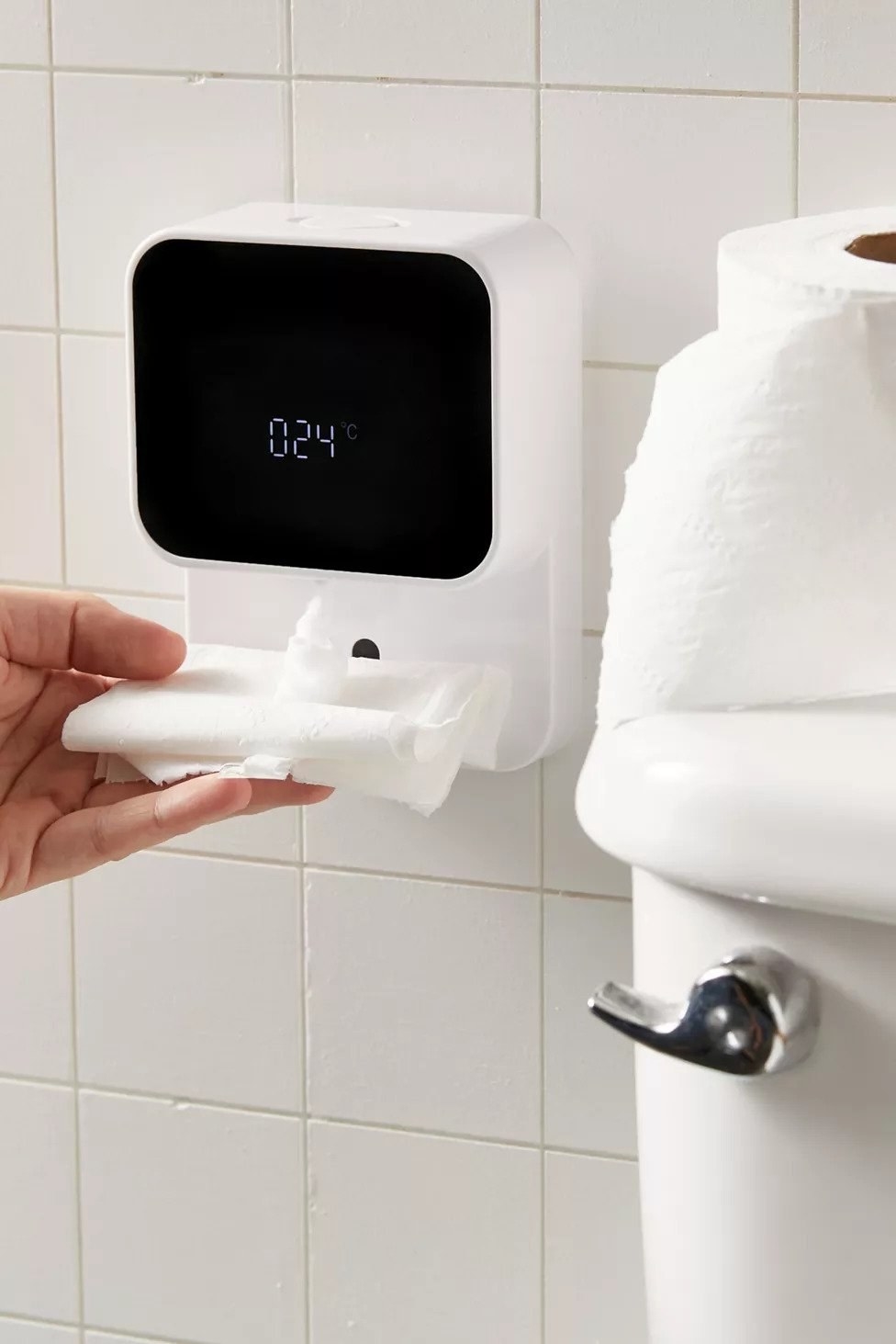 hand holding dry tissue paper under the wall mounted foam dispenser. the screen shows the room's temperature.