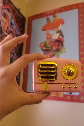 reviewer holding the pale pink palm sized speaker shaped like a retro radio