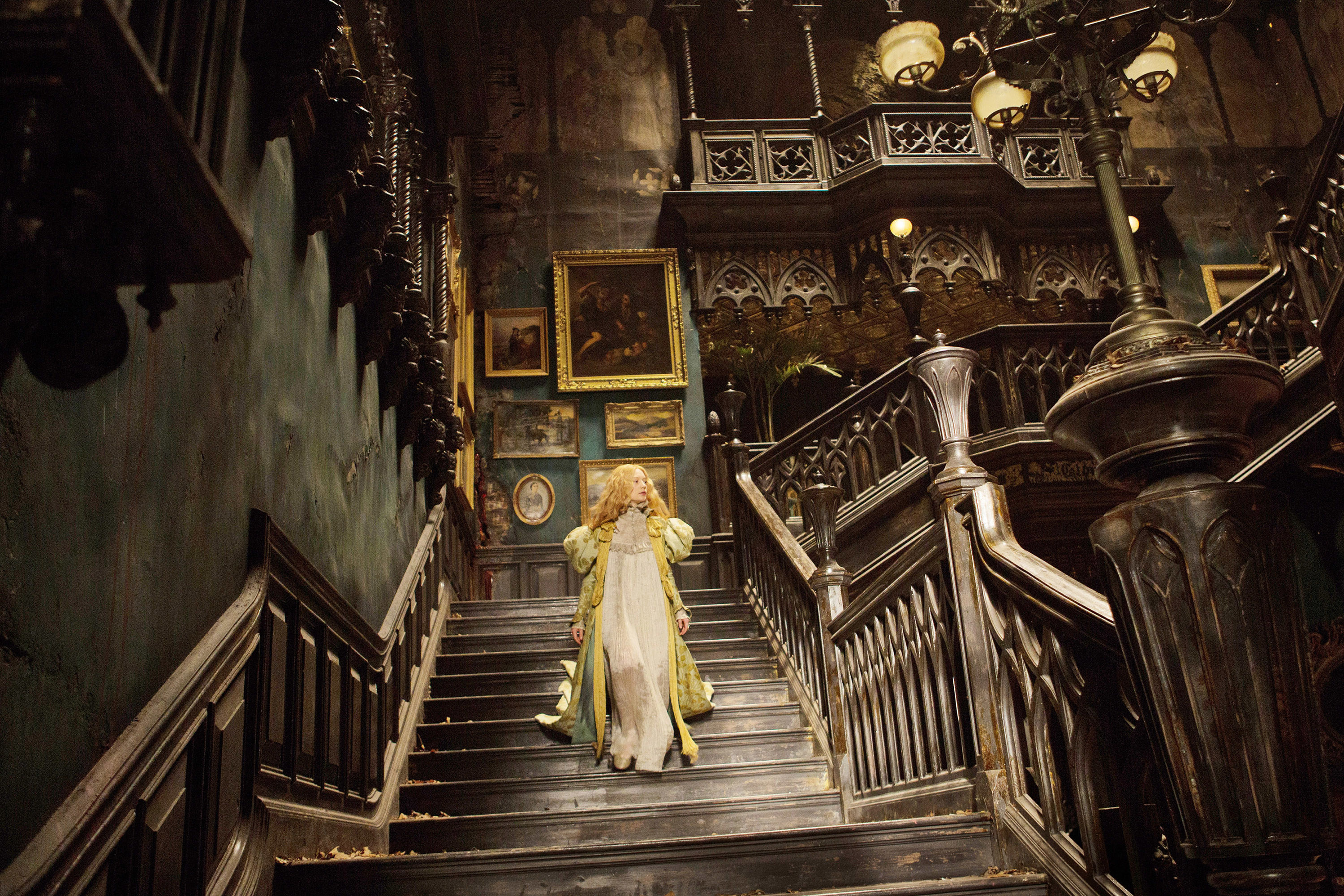 Mia Wasikowska walks down the stairs in a creepy mansion