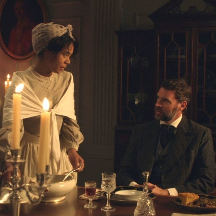 An enslaved woman serving food to a white man in a scene from Due North