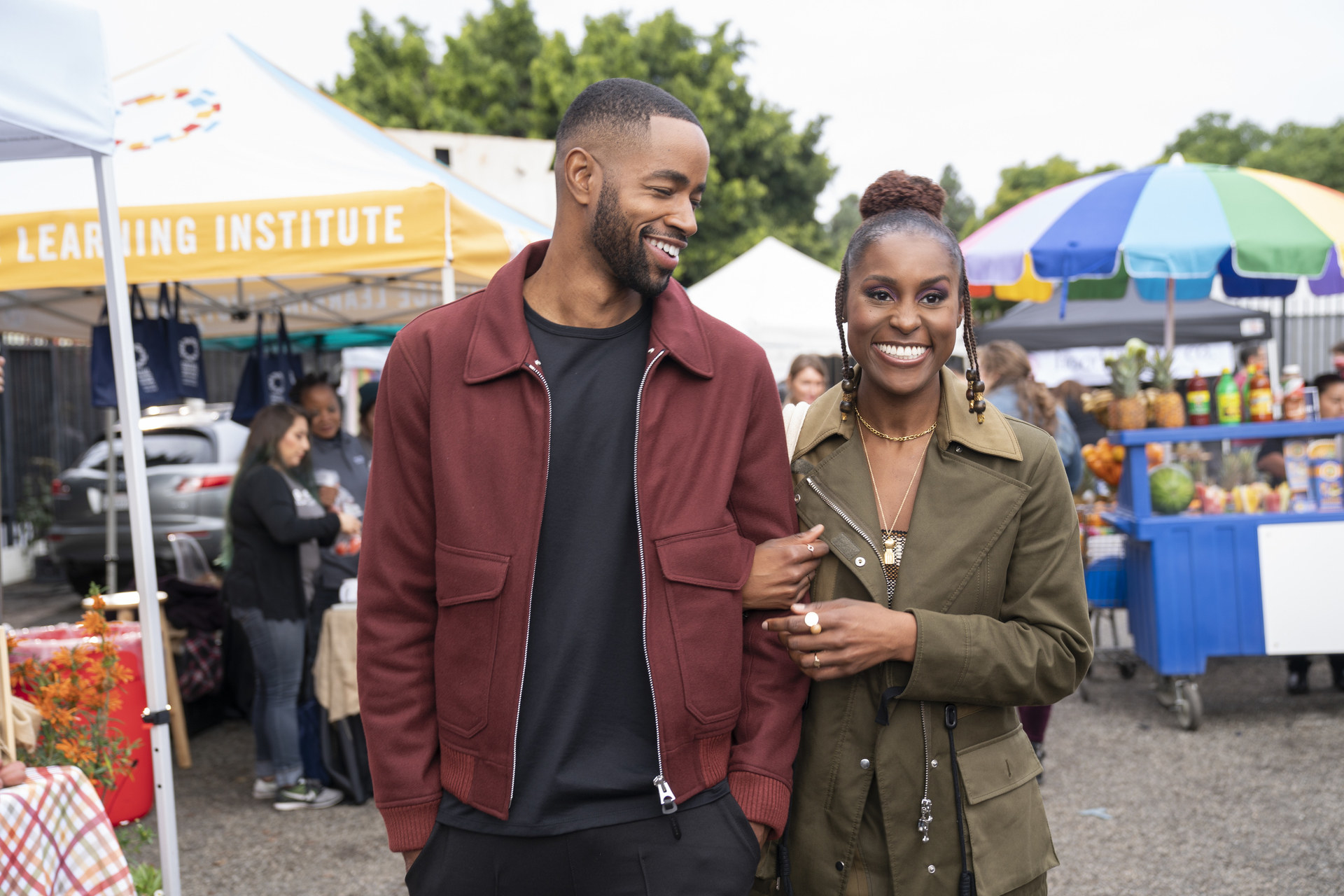 Lawrence and Issa walking through a farmer&#x27;s market arm-in-arm