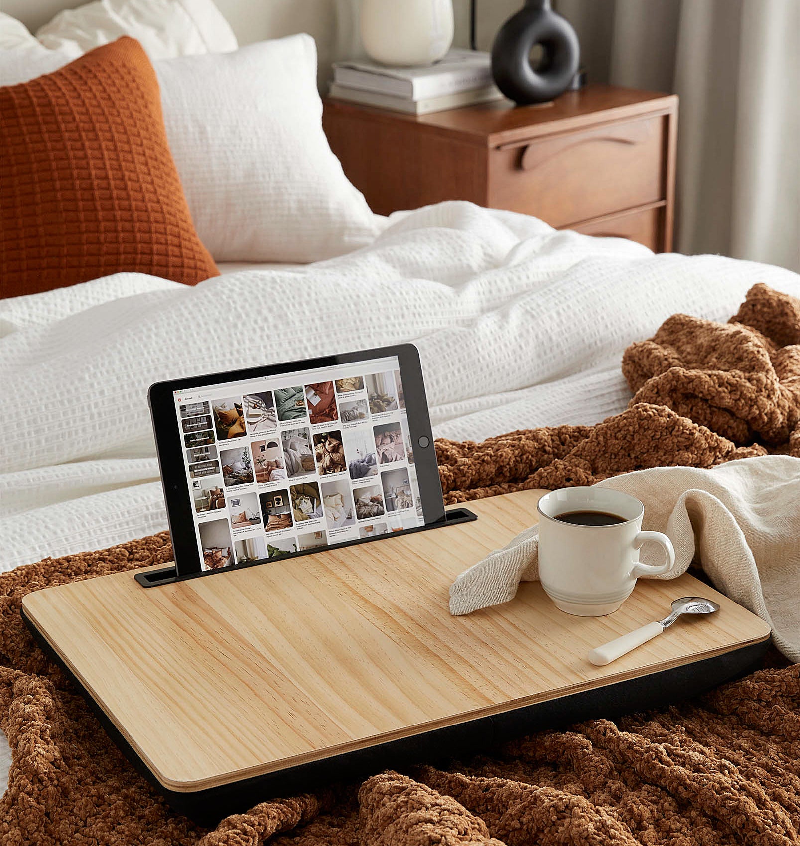 a large laptop tray on a messy bed; a tablet is propped up in the slot