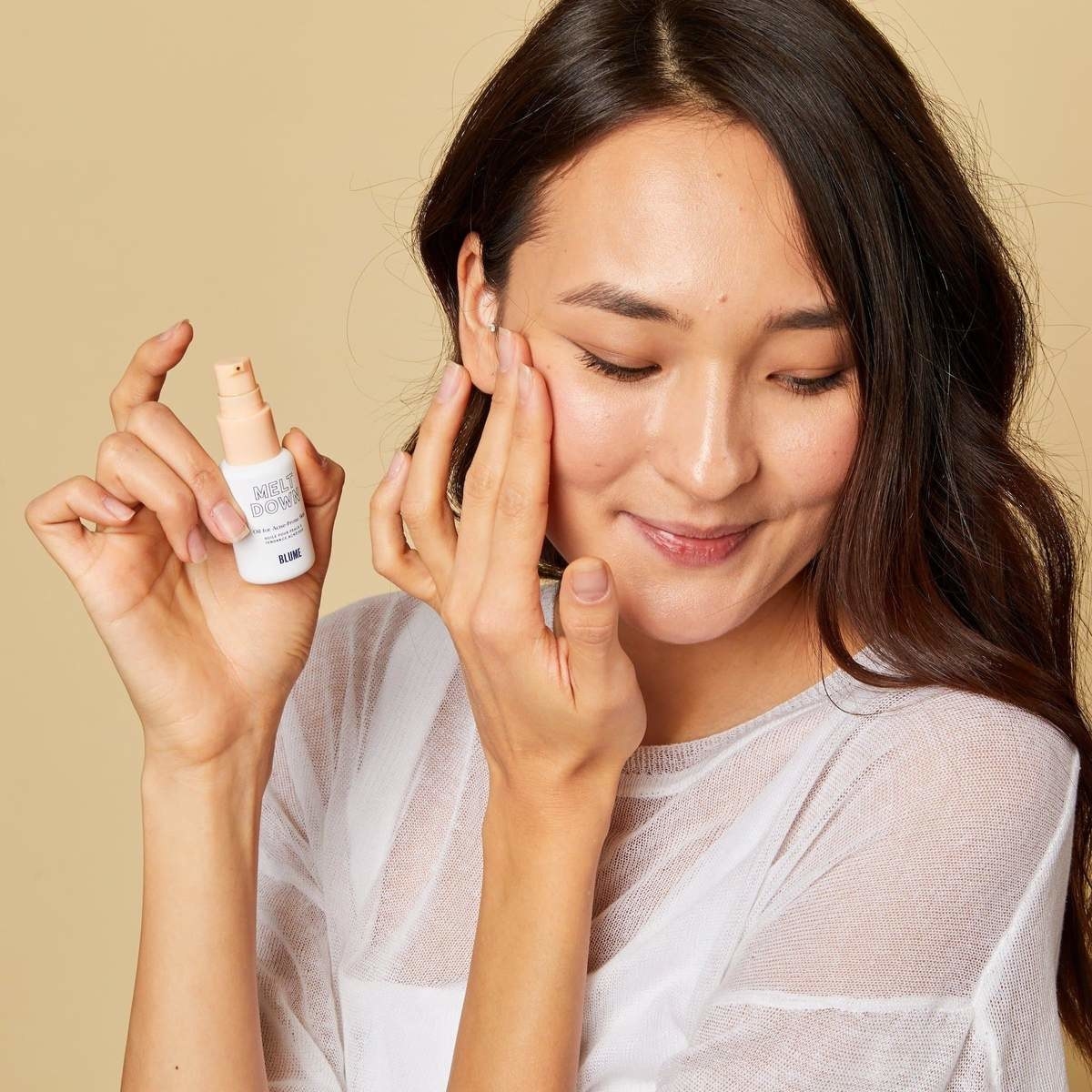model holding the acne oil bottle and applying some of it to her face