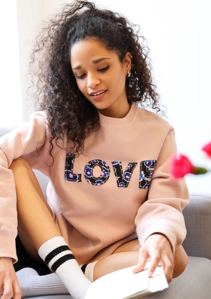 model wearing the pink sweatshirt with floral print letters that spell out &quot;love&quot;