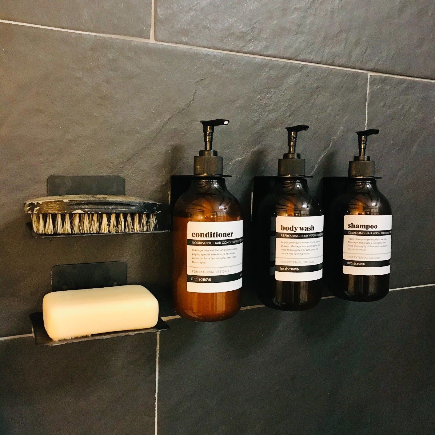 Reviewer&#x27;s shampoo, conditioner, and body wash bottles are shown on the wall of a shower