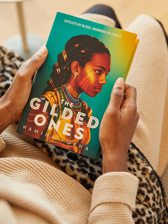 A photo of a person holding &quot;The Gilded Ones,&quot; which has an illustration of a girl on the cover.