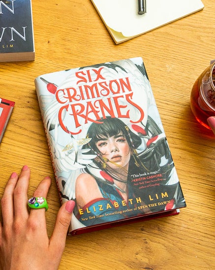 A table with other books and &quot;Six Crimson Cranes,&quot; which has an illustration of a girl surrounded by cranes on the cover.