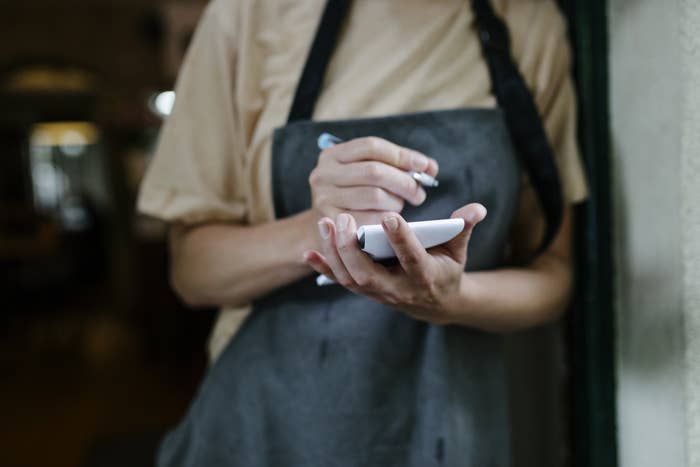 A server standing in the doorway of a restaurant and writing on their notepad.