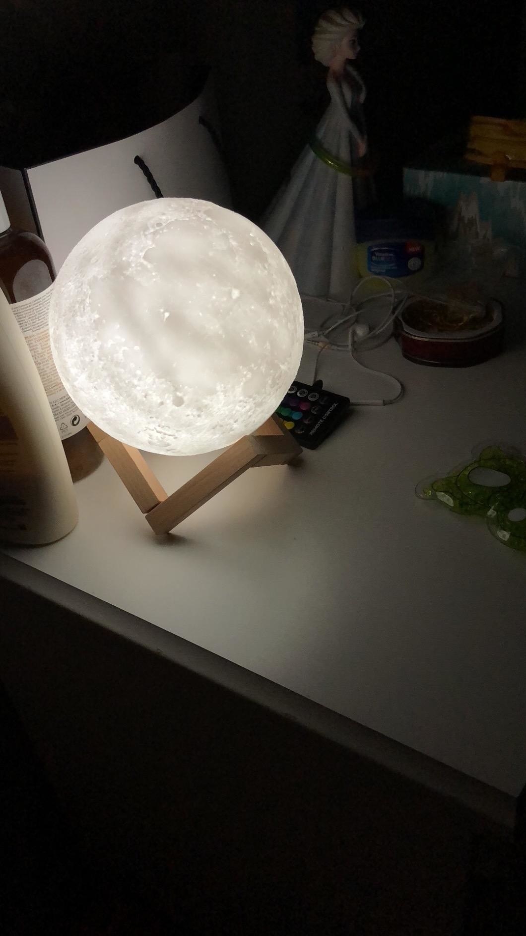 the moon lamp lit up white sitting on its wooden stand