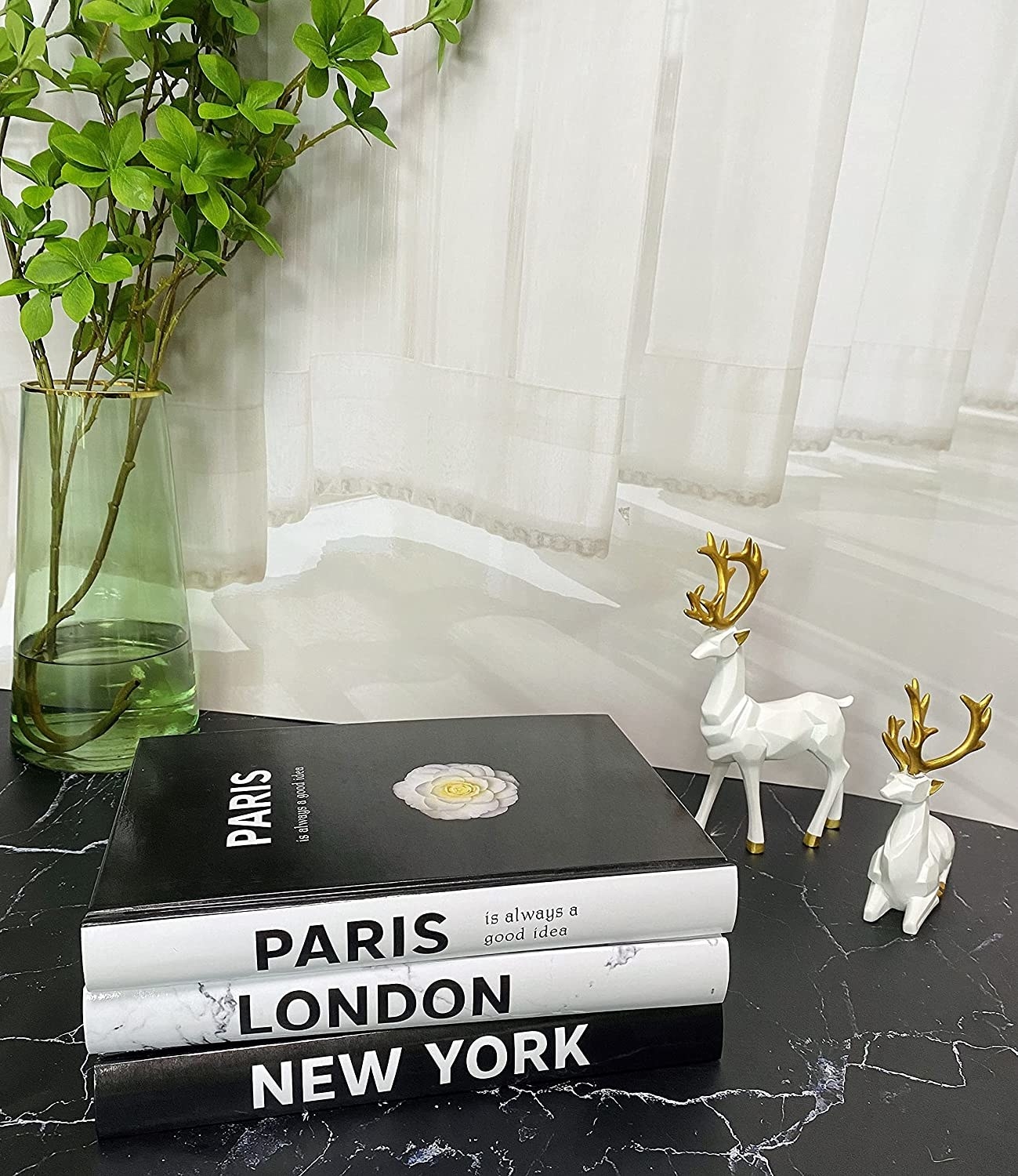 the three books that say &quot;paris&quot; &quot;london&quot; and &quot;new york&quot; stacked on a counter with two ceramic deer standing next to them