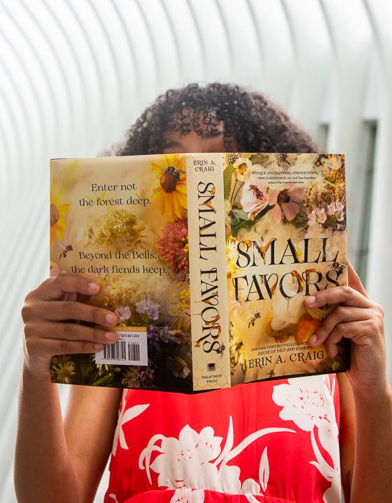 A girl reading &quot;Small Favors,&quot; which has an illustration of flowers and bees.