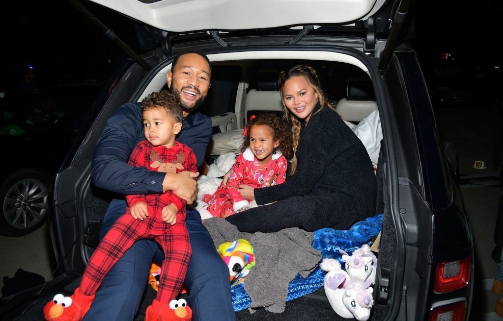 Chrissy and John in the backseat of the car with their two children, who both wear onesie pajamas