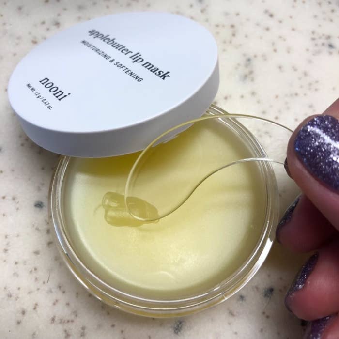 Reviewer holding the included applicator next to an open jar of the lip mask