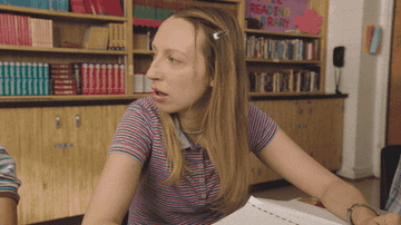 Anna Konkle as Anna Kone sits at a desk as she turns away from her friend in frustration and back to her notebook in &quot;PEN15&quot;