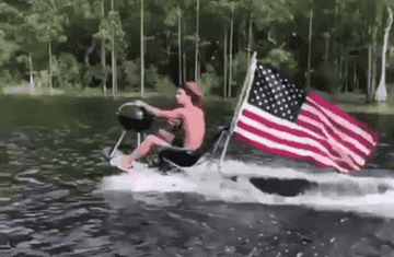 A man rides a jet ski with an American flag flowing in the wind behind it