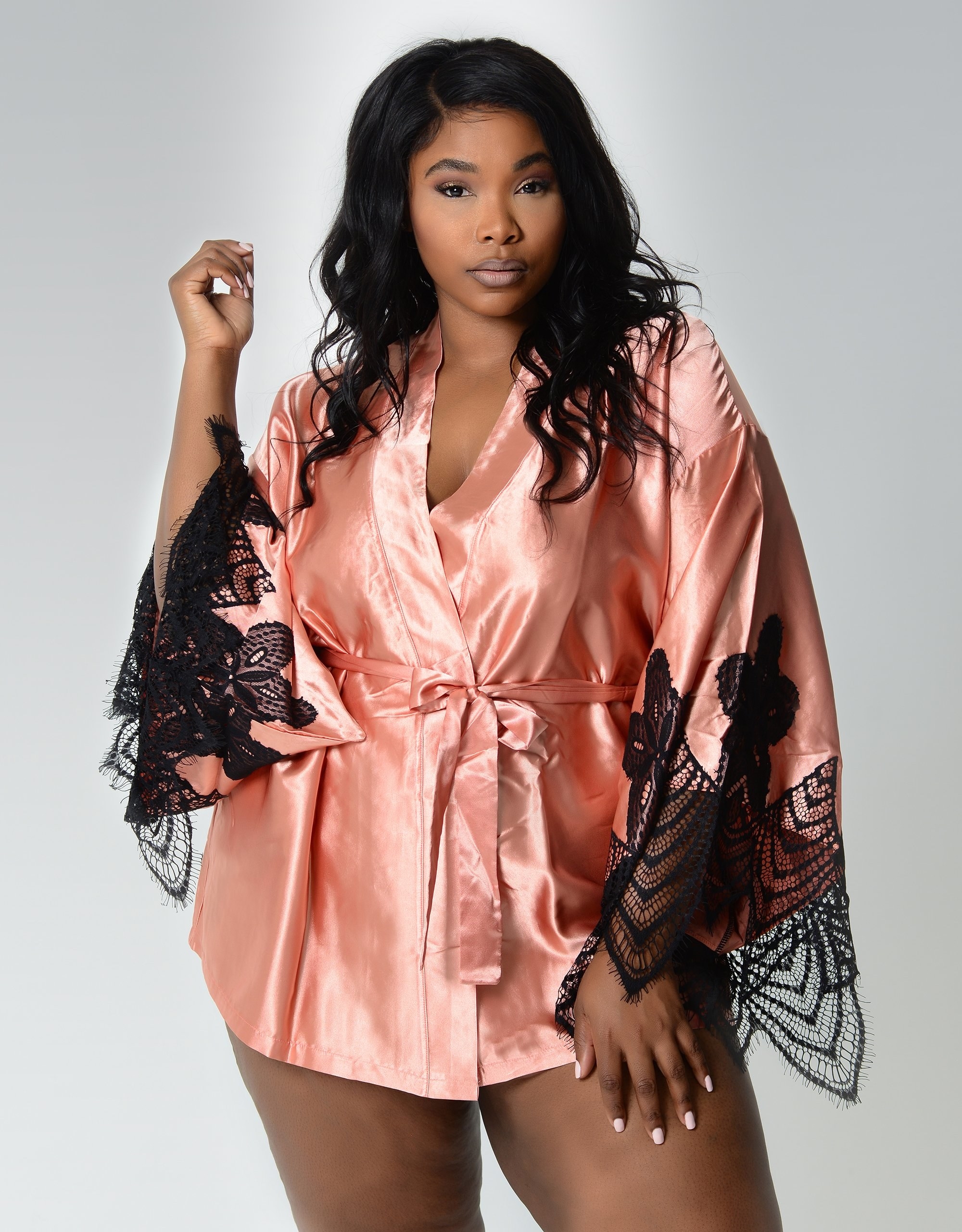 a model in a pink satin robe with black lace sleeve accents